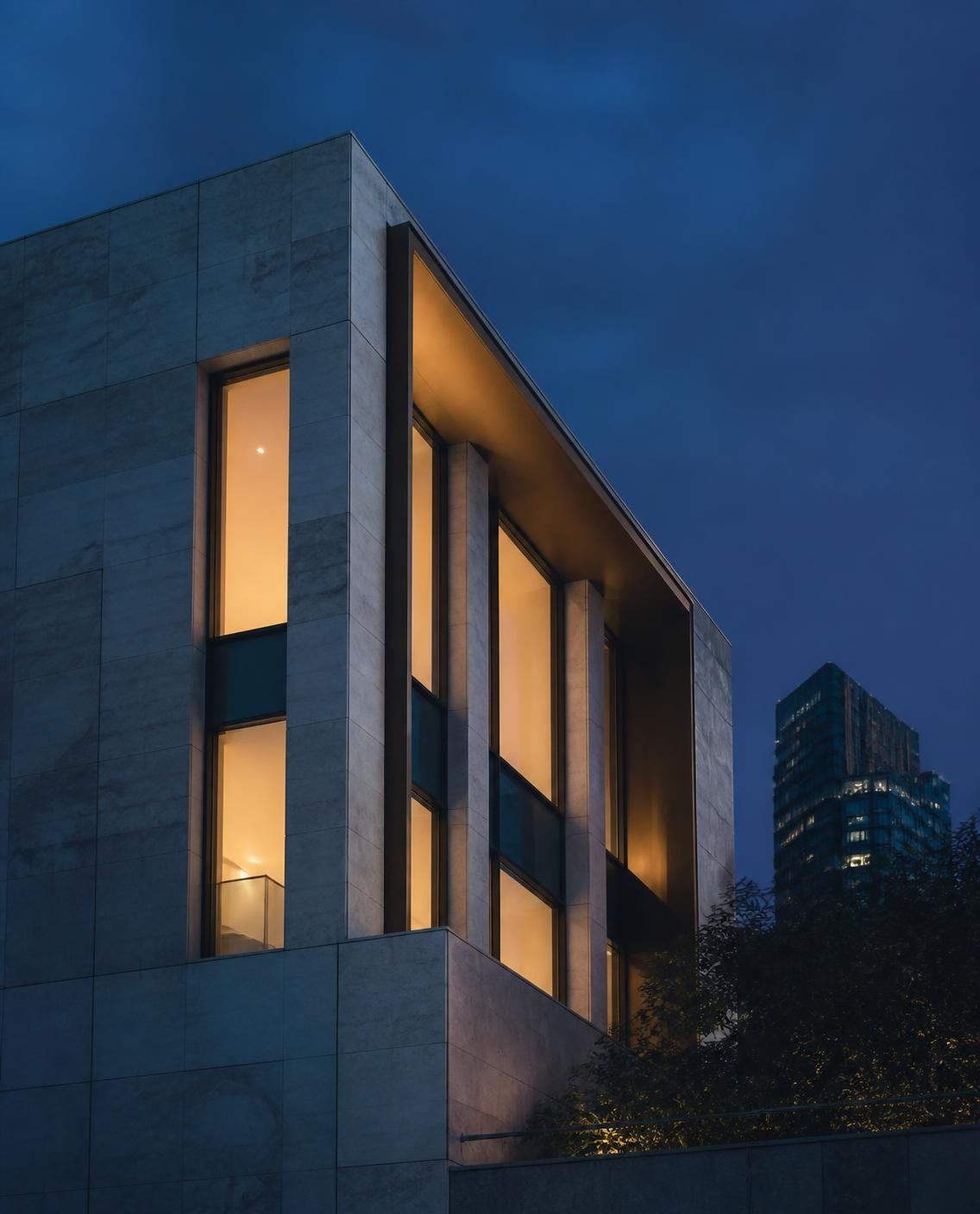 Fachada de piedra y vidrio de un edificio contemporáneo al anochecer, con ventanas iluminadas